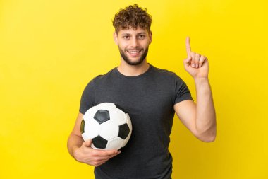 Sarı arka planda izole edilmiş yakışıklı genç futbolcu harika bir fikre işaret ediyor.