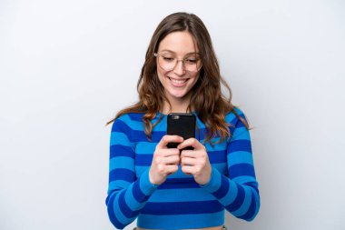 Beyaz arka planda izole edilmiş genç beyaz kadın cep telefonuyla mesaj ya da e-posta gönderiyor.