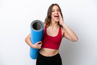 Young sport caucasian woman going to yoga classes while holding a mat isolated on white background shouting with mouth wide open
