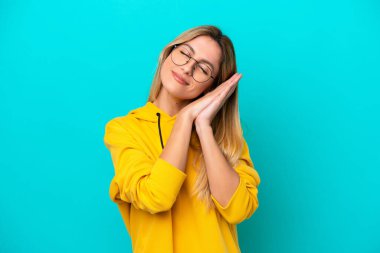 Genç Uruguaylı kadın, mavi arka planda izole edilmiş bir şekilde uyku jesti yapıyor.