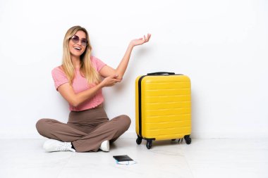 Uruguaylı gezgin kadın, beyaz arka planda izole bir şekilde yerde oturuyor. Gelmesi için ellerini yana uzatıyor.