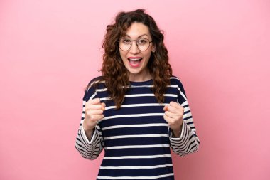 Pembe arka planda izole edilmiş genç beyaz kadın galibiyeti kutluyor.