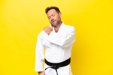Orta yaşlı beyaz bir adam, sarı arka planda karate yapıyor. Çabaladığı için omuz ağrısı çekiyor.