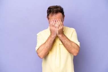 Orta yaşlı beyaz bir adam mor arka planda izole edilmiş, yorgun ve hasta bir ifadeyle.