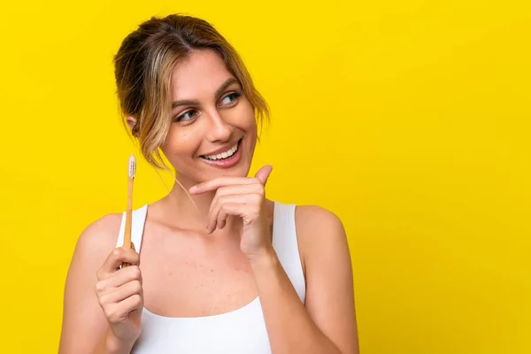 Młoda Urugwajska Kobieta Myjąca Zęby Odizolowana Żółtym Tle Myśląc Pomyśle — Zdjęcie stockowe