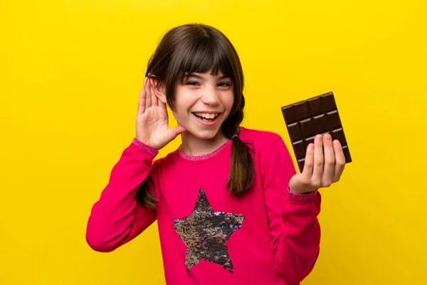 stock image Little caucasian girl with chocolat isolated on yellow background listening to something by putting hand on the ear