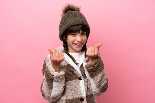一个穿着冬季夹克的高加索小女孩穿着粉色背景的衣服 做着赚钱的姿势 — 图库照片