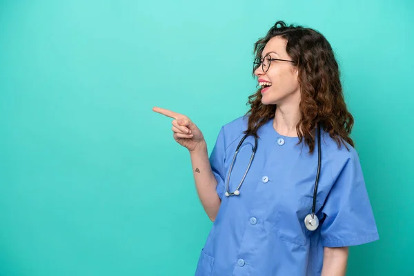年轻的护士高加索女人 被蓝色背景隔离 手指指向侧面 并展示了一种产品 — 图库照片