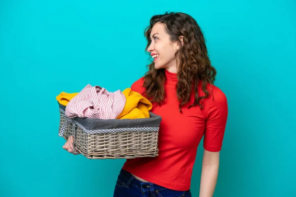 stock image Young caucasian woman holding a clothes basket isolated on blue background laughing in lateral position