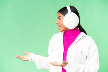 Young African American woman wearing winter muffs over isolated chroma key background with surprise facial expression