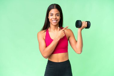 Genç Afrikalı Amerikalı kadın spor kadın halterci izole edilmiş krom anahtar arka plan üzerinde ağırlık kaldırıyor. Bir ürünü sunmak için kenarı işaret ediyor.