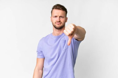 İzole edilmiş beyaz arka planda genç, yakışıklı beyaz bir adam, olumsuz bir ifadeyle baş parmağını aşağı gösteriyor.