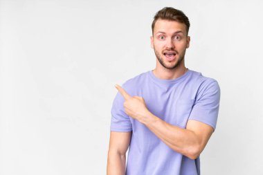 Soyutlanmış beyaz arka planı olan yakışıklı beyaz bir adam şaşırmış ve işaret ediyor.