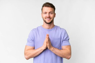 Young handsome caucasian man over isolated white background keeps palm together. Person asks for something