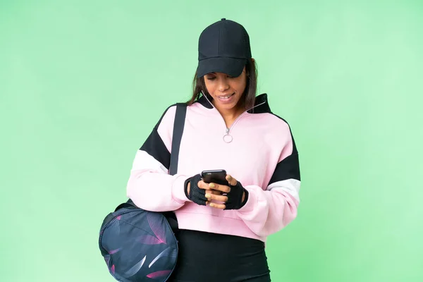年轻的非洲裔美国女子体育袋与孤立的彩色关键背景发送消息与手机 — 图库照片