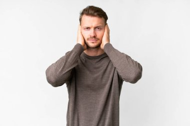 İzole edilmiş beyaz arka planı olan yakışıklı beyaz adam hayal kırıklığına uğramış ve kulaklarını kapatmış.