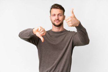 Young handsome caucasian man over isolated white background making good-bad sign. Undecided between yes or not