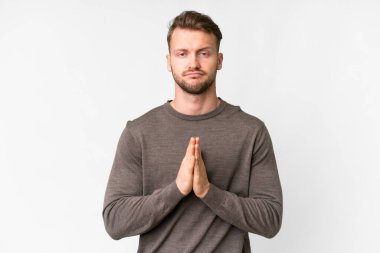 Young handsome caucasian man over isolated white background keeps palm together. Person asks for something