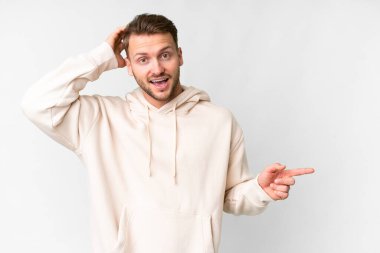 Young handsome caucasian man over isolated white background surprised and pointing finger to the side