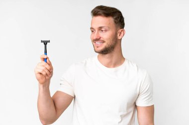 Genç beyaz adam sakalını soyutlanmış beyaz arka planda mutlu bir ifadeyle tıraş ediyor.