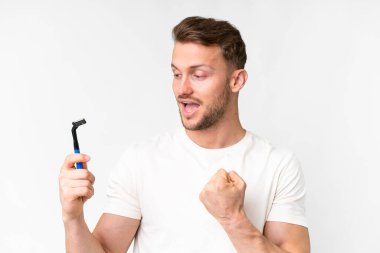 Beyaz arka planda sakalını traş eden genç beyaz bir adam zaferi kutluyor.