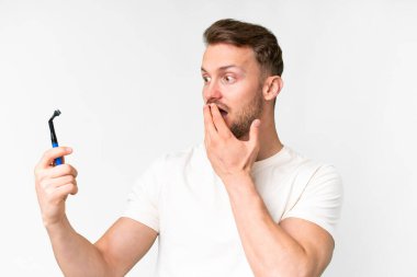 Genç beyaz adam sakalını soyutlanmış beyaz arka planda şaşırtıcı ve şok olmuş bir yüz ifadesiyle tıraş ediyor.