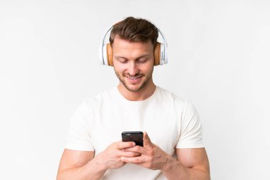 Beyaz arka planda yaşayan yakışıklı beyaz bir adam müzik dinliyor ve cep telefonu arıyor.