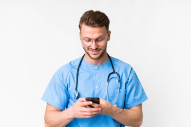 İzole edilmiş beyaz arka planda genç bir hemşire cep telefonuyla mesaj gönderiyor.