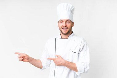 Young caucasian chef over isolated white background surprised and pointing side