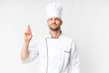 Young caucasian chef over isolated white background with fingers crossing and wishing the best