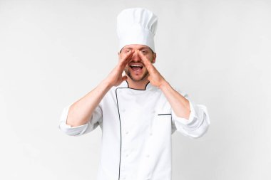 Young caucasian chef over isolated white background shouting and announcing something