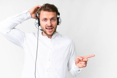 Tele pazarlamacı, beyaz arka planda kulaklıkla çalışan beyaz bir adam şaşırmış ve parmağıyla kenarı işaret ediyor.