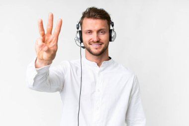 Tele pazarlamacı beyaz arka planda kulaklıkla çalışan beyaz bir adam mutlu ve parmaklarıyla üçe kadar sayıyor.