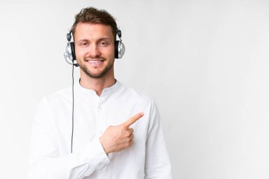 Tele pazarlamacı, beyaz arka plan üzerinde çalışan beyaz kulaklıklı beyaz bir adam bir ürün sunmak için kenarı işaret ediyor.