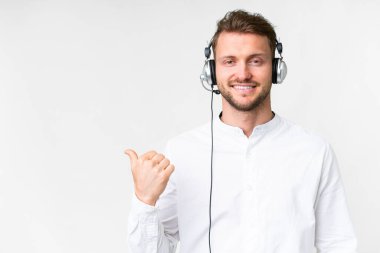 Tele pazarlamacı, beyaz arka plan üzerinde çalışan beyaz kulaklıklı beyaz bir adam bir ürün sunmak için kenarı işaret ediyor.