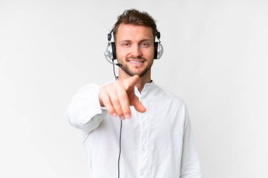 Tele pazarlamacı, beyaz arka planda kulaklıkla çalışan beyaz bir adam kendine güvenen bir ifadeyle sana işaret ediyor.