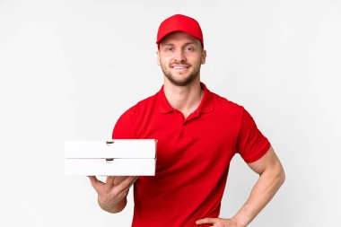 Pizza delivery man with work uniform picking up pizza boxes over isolated white background posing with arms at hip and smiling