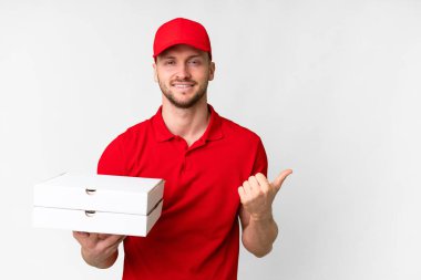 İş üniformalı bir pizzacı, izole edilmiş beyaz arka planda pizza kutularını topluyor ve bir ürün sunmak için yan tarafı işaret ediyor.