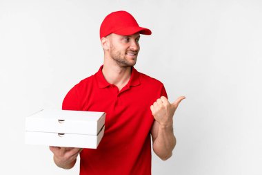 Pizza delivery man with work uniform picking up pizza boxes over isolated white background pointing to the side to present a product