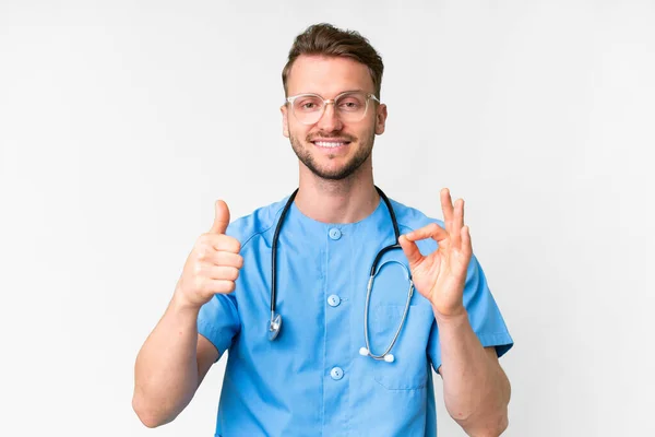 年轻的护士男子在孤独的白种人背景上表现出良好的体征和大拇指向上的姿势 — 图库照片