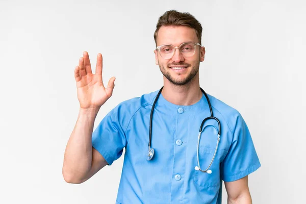 Junger Krankenpfleger Vor Isoliertem Weißen Hintergrund Salutiert Mit Glücklicher Miene — Stockfoto