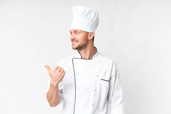 年轻的高加索厨师通过孤立的白色背景指向侧面来展示一种产品 — 图库照片