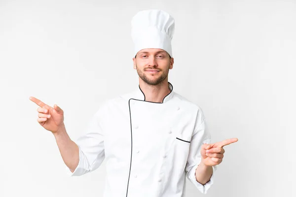 Young Caucasian Chef Isolated White Background Pointing Finger Laterals Happy — Zdjęcie stockowe