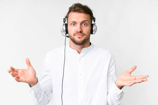 一个高加索人 头戴耳机 在孤立的白色背景上工作 一边举手表决 一边怀疑 — 图库照片