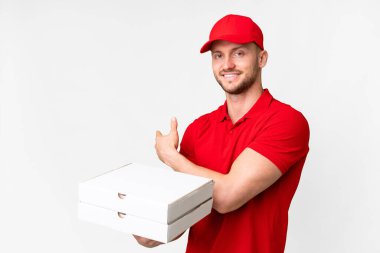 Pizza delivery man with work uniform picking up pizza boxes over isolated white background pointing back