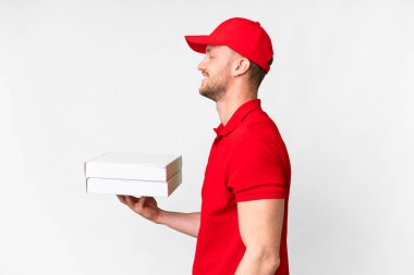 Pizza delivery man with work uniform picking up pizza boxes over isolated white background laughing in lateral position