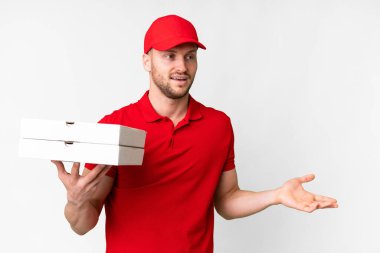 Pizza delivery man with work uniform picking up pizza boxes over isolated white background with surprise expression while looking side