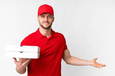Pizza teslimatçısı üniformalı adam izole edilmiş beyaz arka planda pizza kutuları alıyor. Davet etmek için ellerini yana uzatıyor.