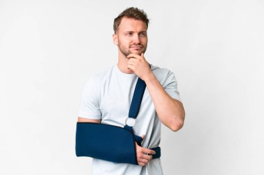 Kırık kollu ve soyutlanmış beyaz arka planda askı takan genç, beyaz bir adam.