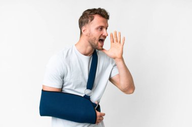 Kırık kollu, beyaz arka planda askı takmış ağzı sonuna kadar açık bağıran genç beyaz bir adam.